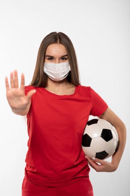 Female football player with mask holding ball and showing stop sign