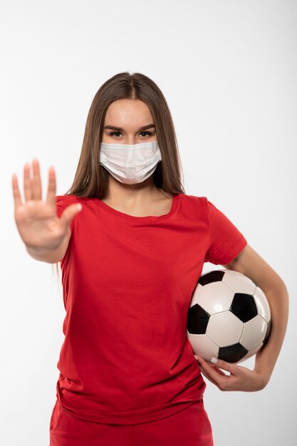 Female football player with mask holding ball and showing stop sign