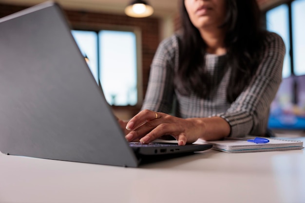 Female freelancer working on report at home, typing research information on laptop and browsing internet website. Searching data to create professional report and send email. Close up.