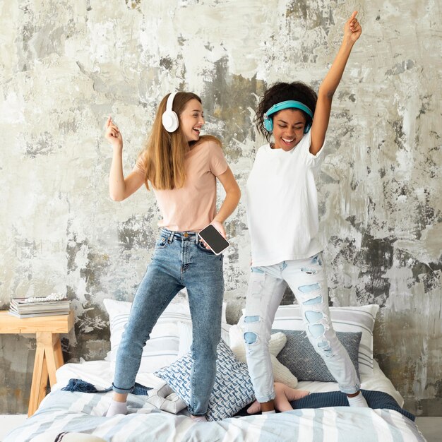 female friends dancing in bed while listening to music on headphones