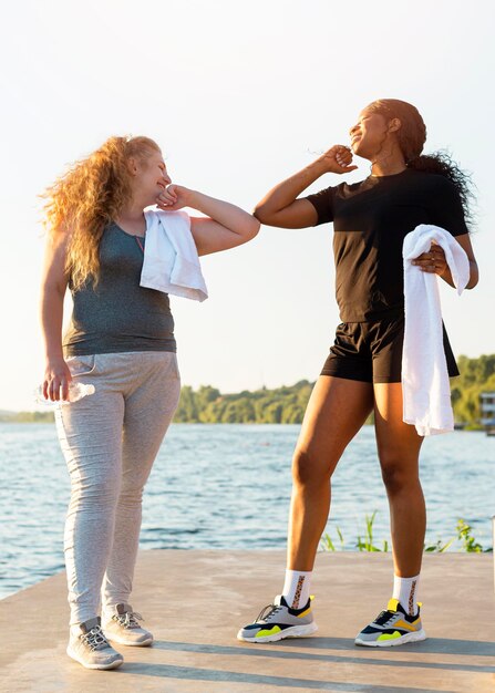 Female friends doing the elbow salute while exercising by the lake