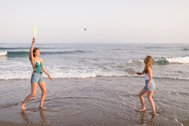 Amici femminili che godono giocando con il tennis alla spiaggia