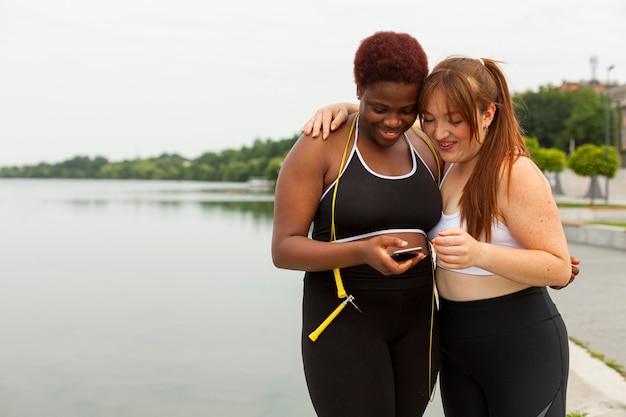 Female friends exercising outdoors and looking at smartphone