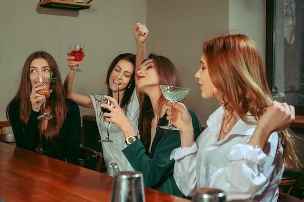 Amici femminili che hanno un drink al bar. sono seduti a un tavolo di legno con cocktail. sono bicchieri tintinnanti