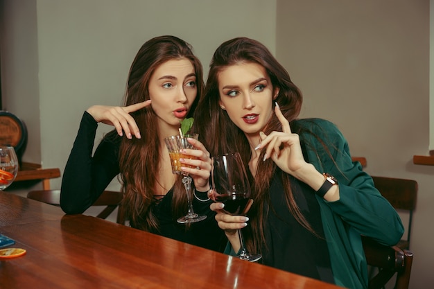 Amici femminili che hanno un drink al bar. sono seduti a un tavolo di legno con cocktail. indossano abiti casual.