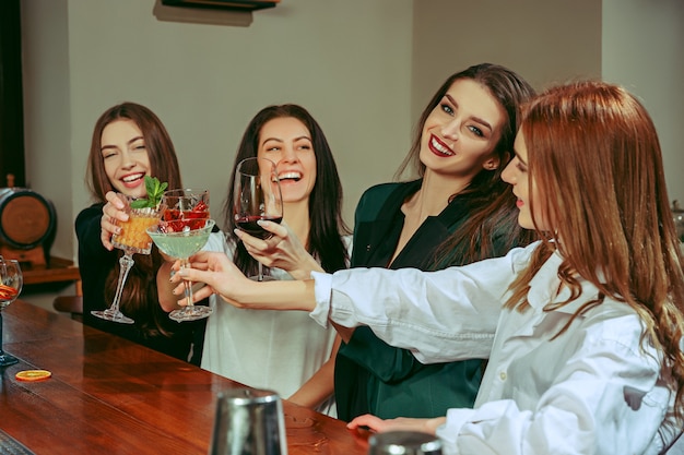 Foto gratuita amici femminili che hanno un drink al bar. sono seduti a un tavolo di legno con cocktail.