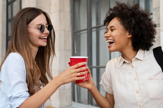 Подруги веселятся вместе на открытом воздухе с пластиковыми стаканчиками
