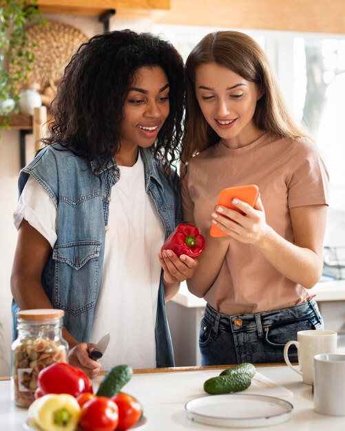 スマートフォンと野菜を持ったキッチンの女友達