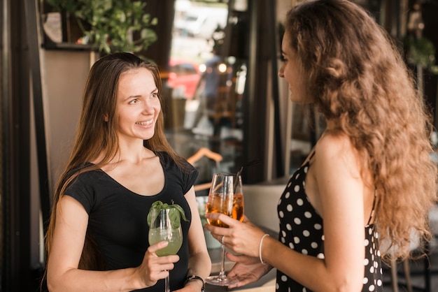 Женщины-друзья, глядя друг на друга, держа стаканы напитков