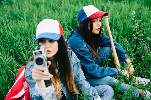 Female friends sitting in field in colored caps and jeans