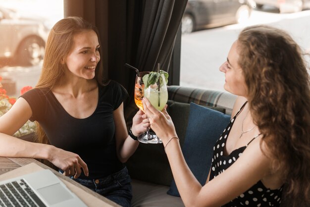 Женщины-друзья, сидящие в ресторане, жарящие бокалы коктейлей
