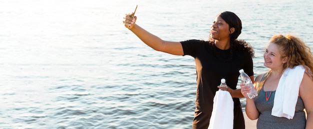 Amici femminili che prendono selfie mentre esercitano in riva al lago
