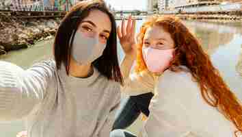 Free photo female friends with face masks outdoors taking a selfie together