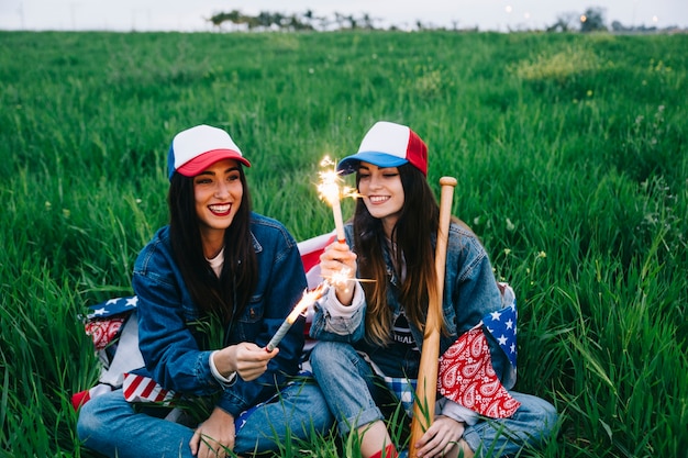 Female friends with fireworks sitting in field