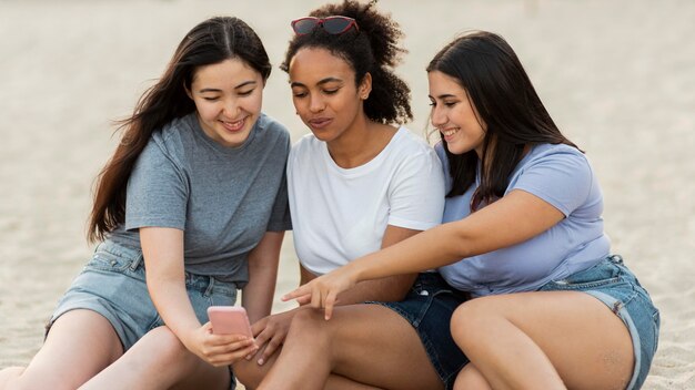 Female friends with smartphone sitting on the beach together