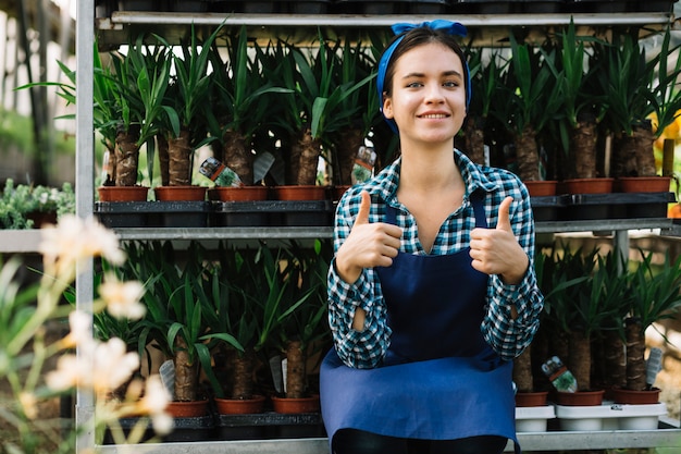 Female gardener gesturing thumbs up in front of potted plants