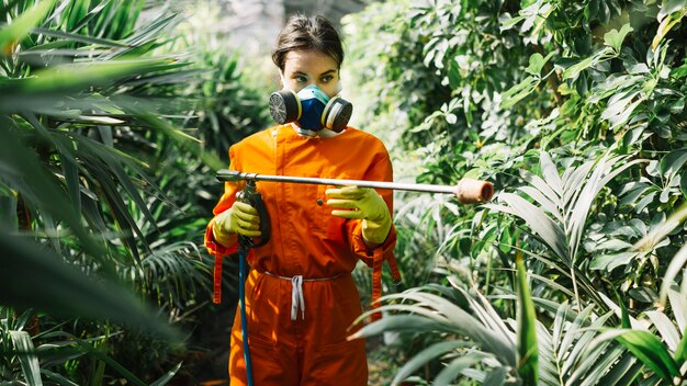 Женский садовник, распыляющий инсектицид на растении
