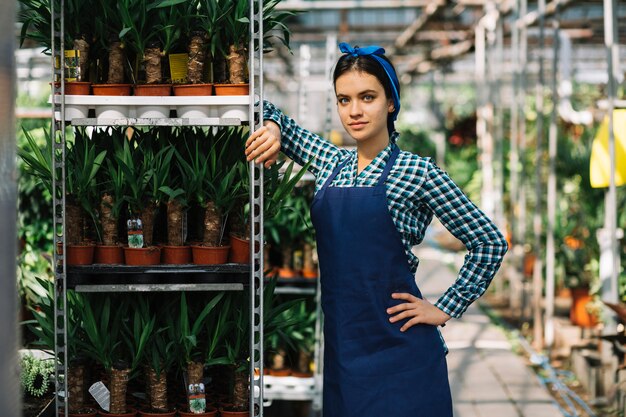 温室内の鉢植えのラックの近くに立つ女性の庭師