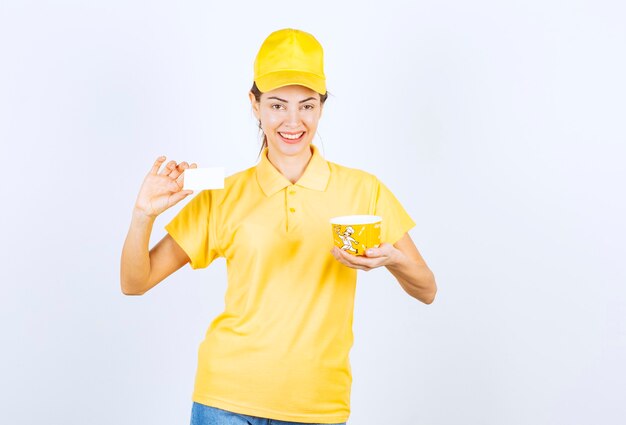 Female girl in yellow uniform delivering a yellow takeaway noodle cup and presenting her business card to the customer. 