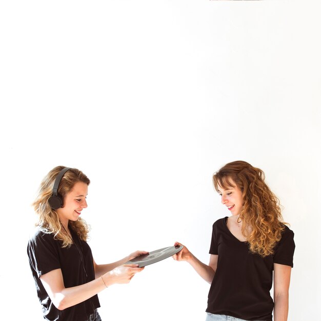 Female giving vinyl record to her sister wearing headphone over white backdrop