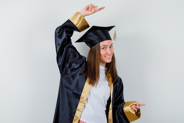 Female graduate in academic dress pointing right and looking cheery , front view.