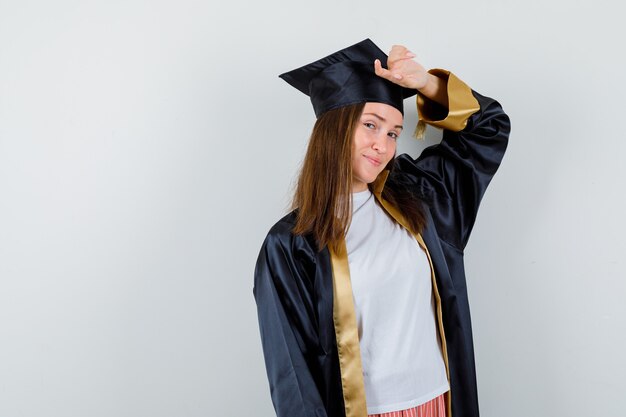 Female graduate posing with hand on head in uniform, casual clothes and looking alluring. front view.