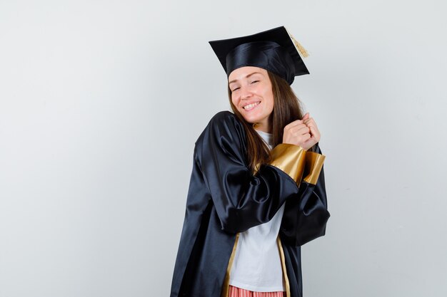 Foto gratuita laureato femminile in posa con le mani tenute insieme in uniforme, abiti casual e allegri, vista frontale.