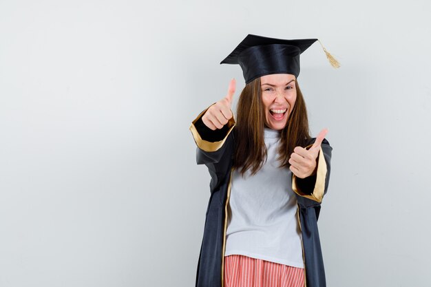 Female graduate showing double thumbs up in uniform, casual clothes and looking happy. front view.