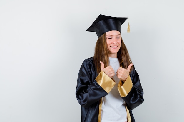 Female graduate showing double thumbs up in uniform, casual clothes and looking lucky , front view.