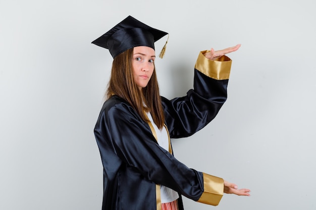 Female graduate showing large size sign in academic dress and looking confident , front view.