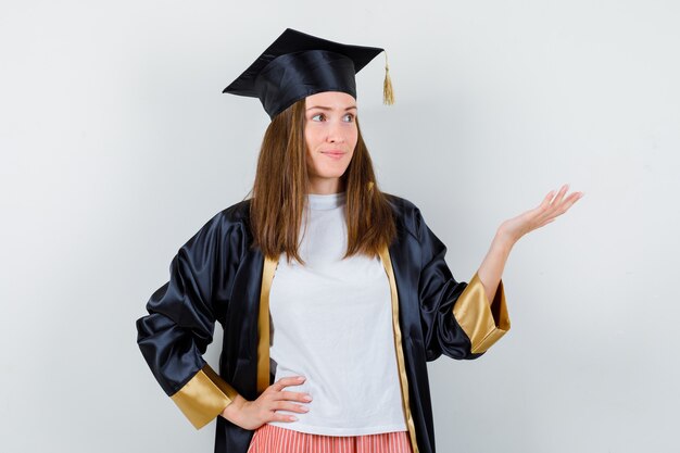 Выпускница-женщина показывает приветственный жест в униформе, повседневной одежде и выглядит сосредоточенной. передний план.