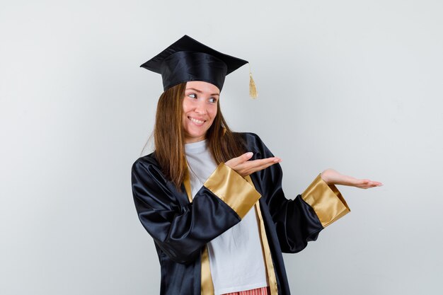 Выпускница-женщина показывает приветственный жест в униформе, повседневной одежде и выглядит весело, вид спереди.