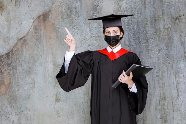 Female graduate student in mask standing over gray wall. High quality photo