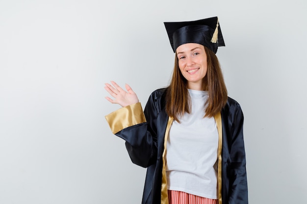 Foto gratuita laureato femminile agitando la mano per il saluto in uniforme, abbigliamento casual e guardando gioioso, vista frontale.