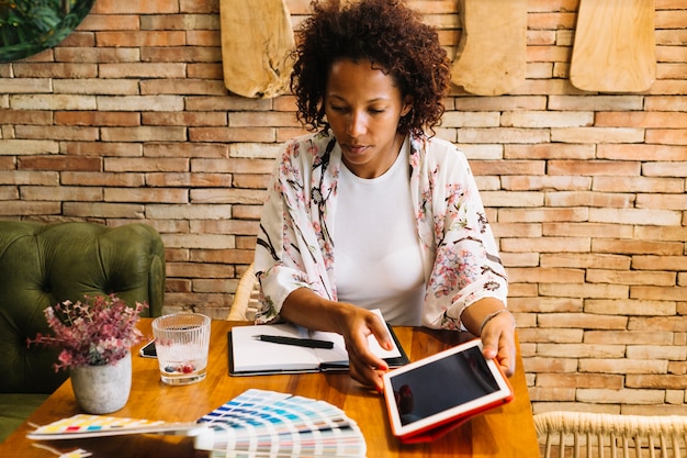 Free photo female graphic designer looking at color swatches holding digital tablet in hand