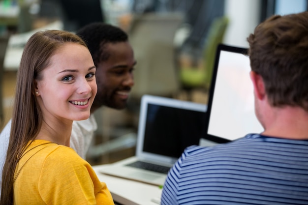 Female graphic designer smiling at camera while colleagues interacting with each other