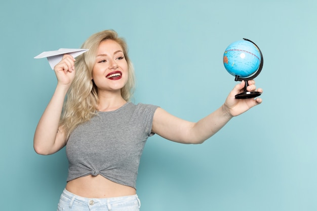 female in grey shirt and bright blue jeans holdign paper plane and little globe