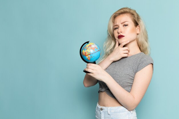 female in grey shirt and bright blue jeans holding little globe