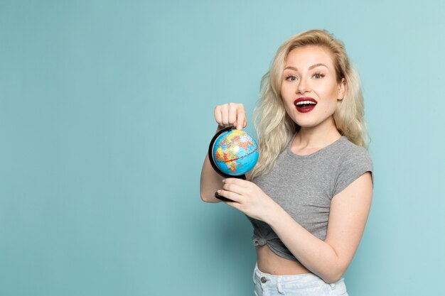 female in grey shirt and bright blue jeans holding little globe