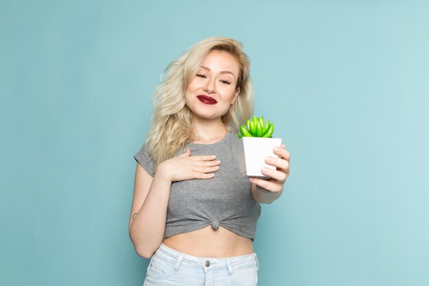 female in grey shirt and bright blue jeans holding little plant
