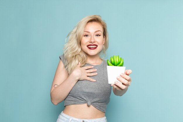 female in grey shirt and bright blue jeans holding little plant