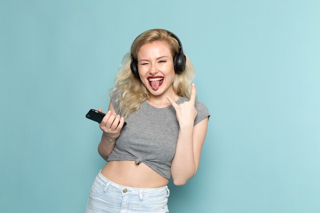 female in grey shirt and bright blue jeans holding a phone with rocker expression