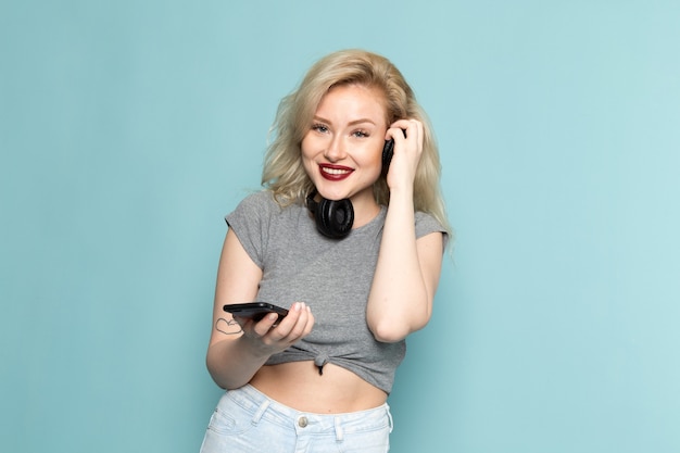 female in grey shirt and bright blue jeans holding a phone