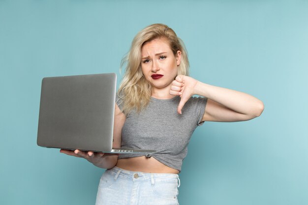 female in grey shirt and bright blue jeans holding silver laptop