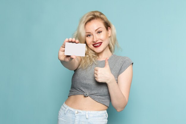 female in grey shirt and bright blue jeans holding white card