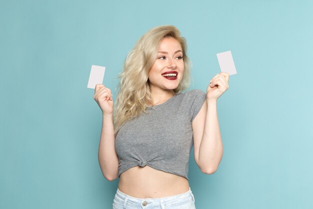 female in grey shirt and bright blue jeans holding white cards