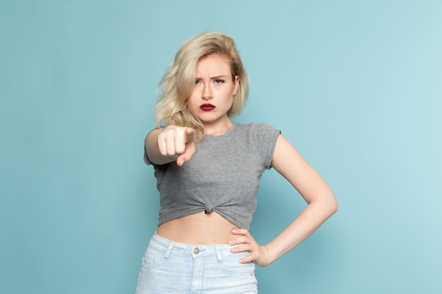 Foto gratuita femmina in camicia grigia e blue jeans luminosi in posa con espressione pazza