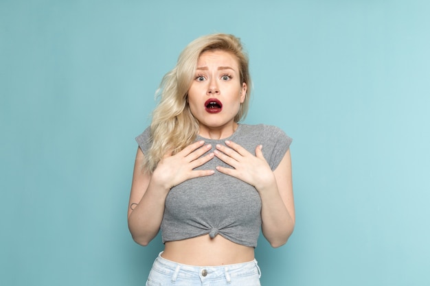 female in grey shirt and bright blue jeans posing with scared expression