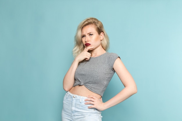 female in grey shirt and bright blue jeans posing with thinking expression