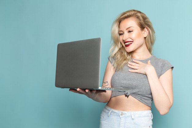 female in grey shirt and bright blue jeans using a laptop